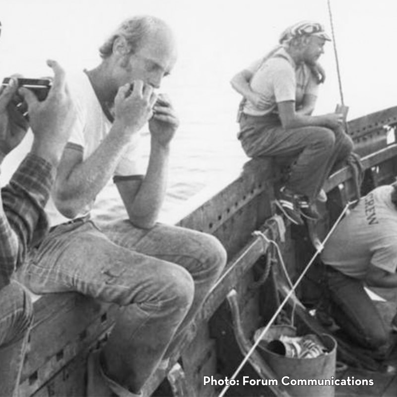 The Hjemkomst's Mark Hilde, Bjorn Holtet, and Deb Asp sitting on the ship's deck. Hilde and an unidentified crew member play harmonica (Photo: Forum Communications).Picture