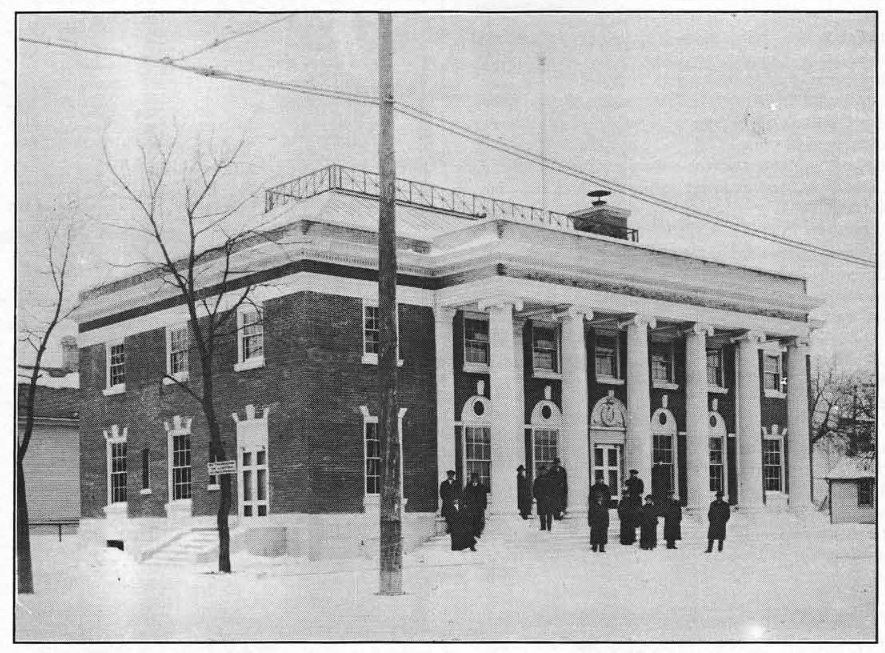 Image: a winter photograph of twelve people standing outside of the Moorhead Post Office in 1915.