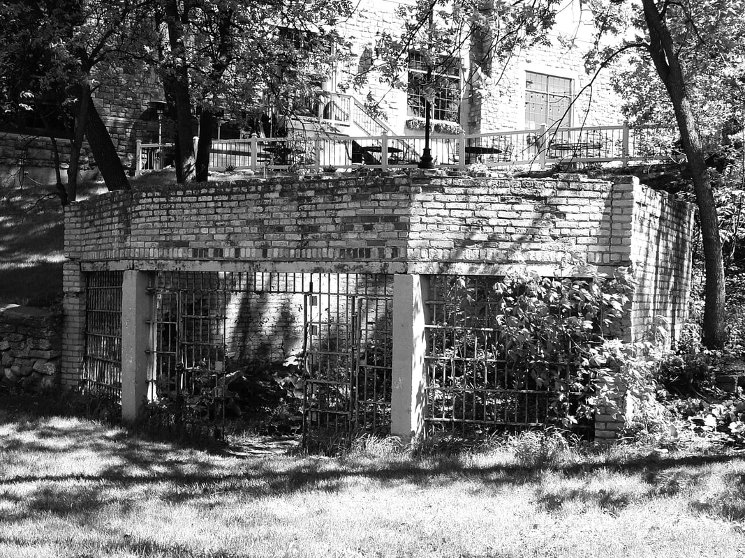 Image: a black and white photograph of the remains of the Moorhead Zoo's bear cage below the former Usher's House location.