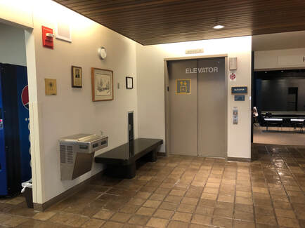 Interior photo of museum showing a bench, water fountain, and elevator.